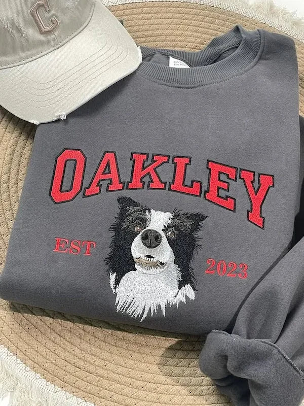 Charcoal Oakley dog portrait sweatshirt beside a neutral cap