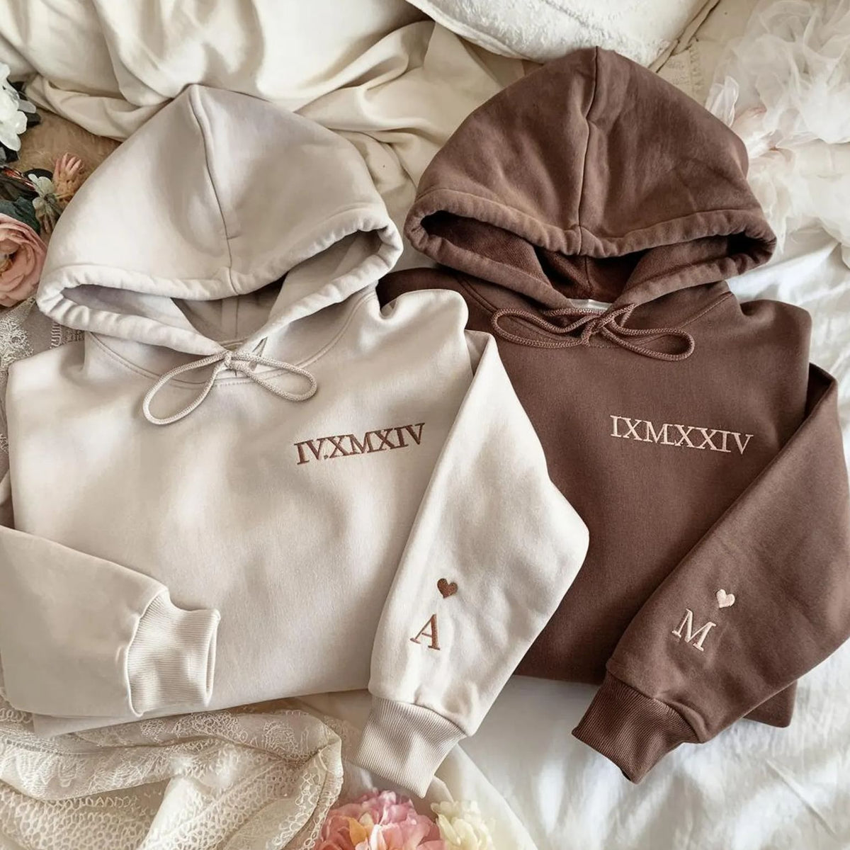 Cream and brown personalized date hoodies laid together on a soft blanket