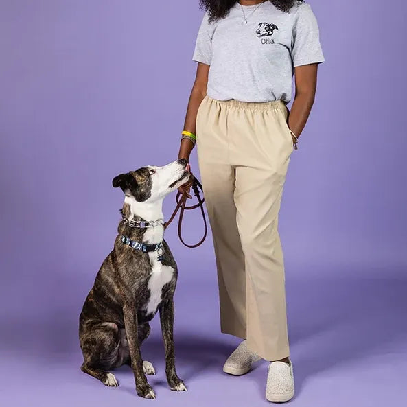 Woman in a white tee with a left chest line art dog portrait and the name Captain, standing with her brindle dog