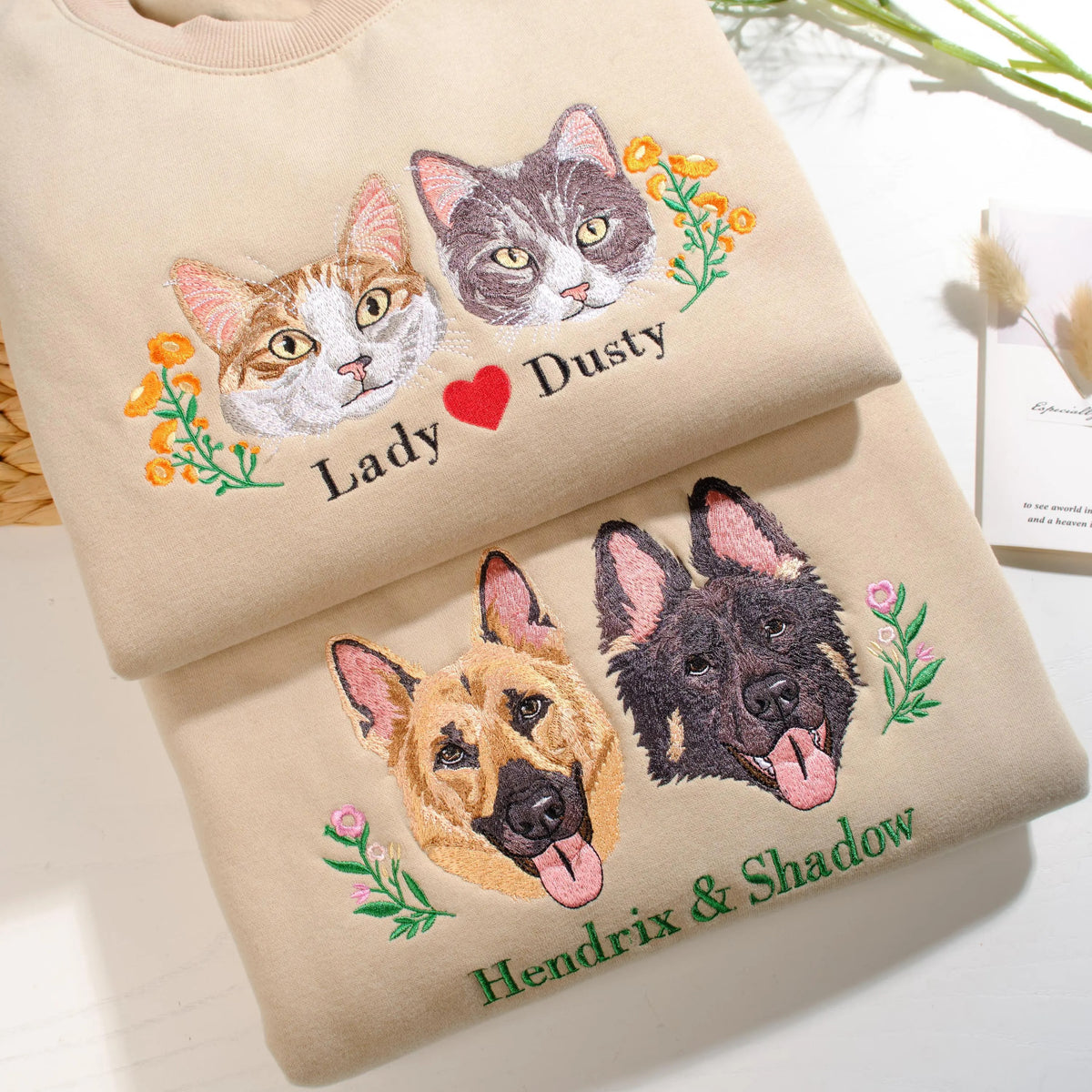 Two folded beige sweatshirts with personalized cat and German shepherd portrait designs