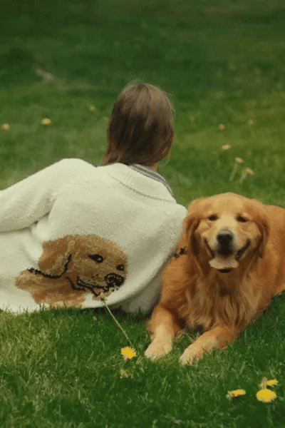 Woman in a light sage cardigan with a golden retriever knitted on the back, relaxing on the grass beside her dog