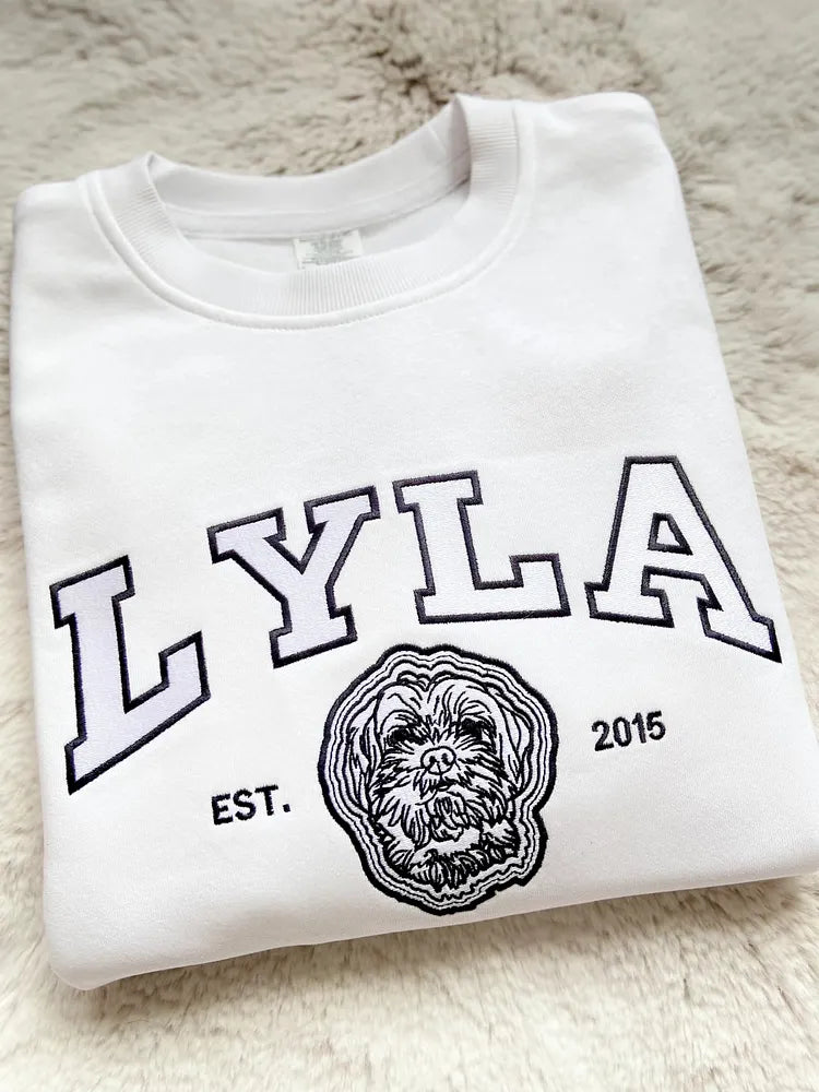 White sweatshirt with LYLA in outlined varsity letters above a black embroidered dog outline