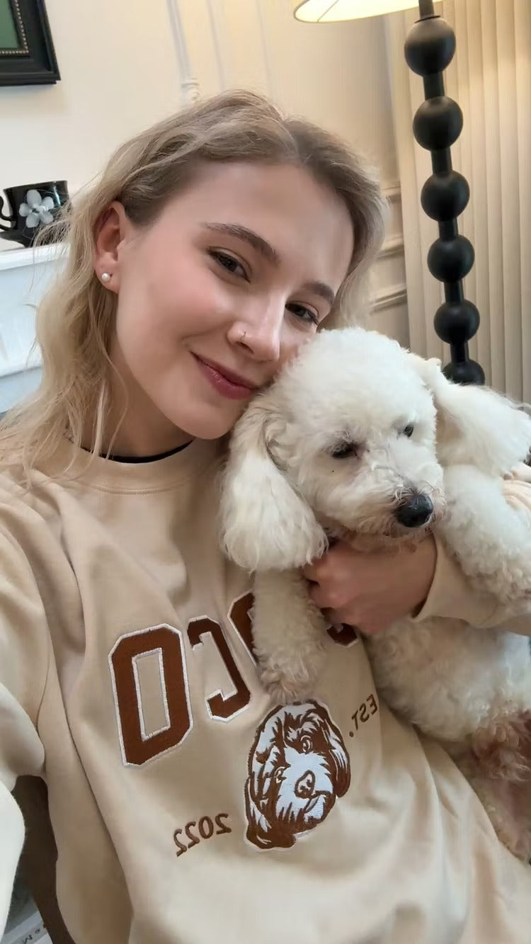Woman cuddling a white poodle while wearing a cream COCO sweatshirt