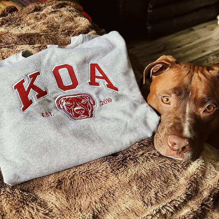 Pit bull lying next to a gray sweatshirt with KOA in red letters and a pit bull outline
