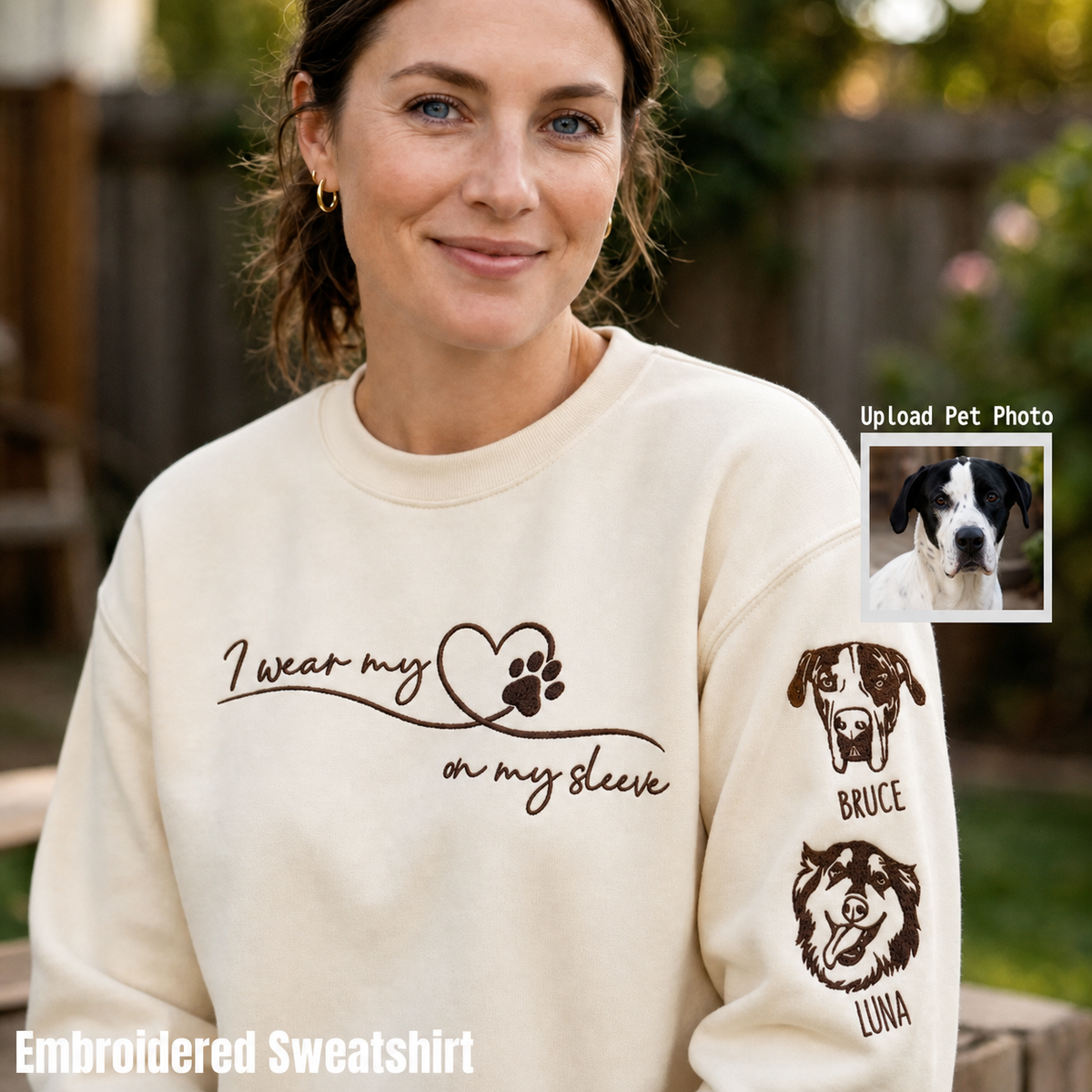 Woman in a cream sweatshirt embroidered with “I wear my heart on my sleeve” and two dog portraits with names down the sleeve