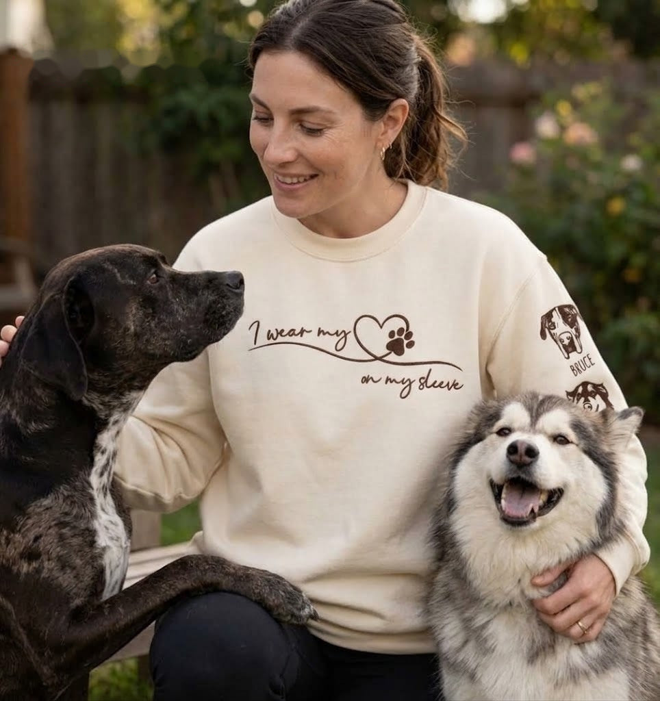 Woman in a cream heart-on-my-sleeve sweatshirt petting her two dogs